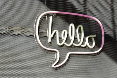 A pink neon sign the reads hello hangs on a wall during the day.